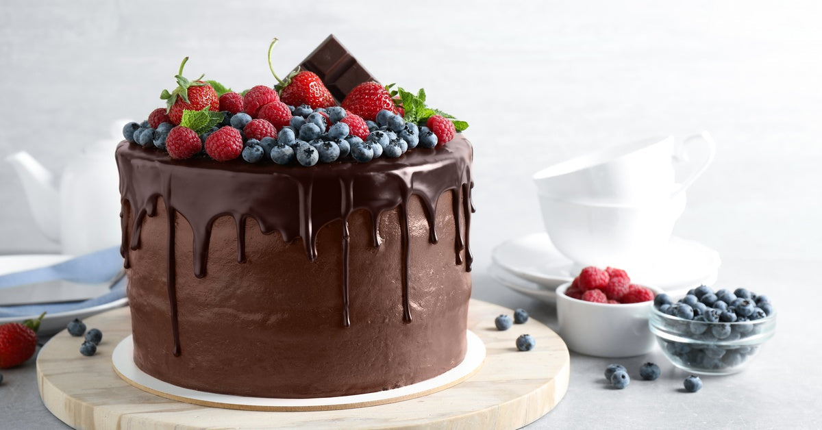 A chocolate cake decorated with a chocolate drip glaze, fresh fruit, and a bar of chocolate on top.