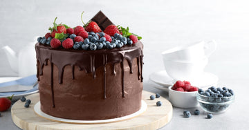 A chocolate cake decorated with a chocolate drip glaze, fresh fruit, and a bar of chocolate on top.